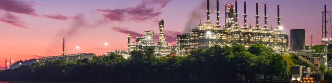 A tranquil sunset setting showcasing Shell Polymer's Monaca, PA plant amidst a backdrop of water and lush trees, creating a captivating sight