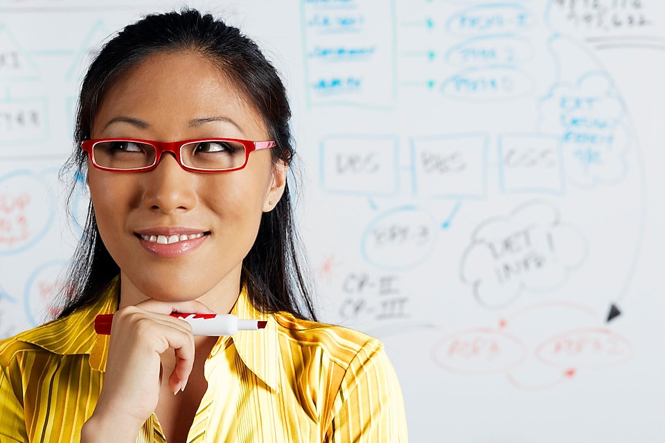 A woman is working on a white board and smiling