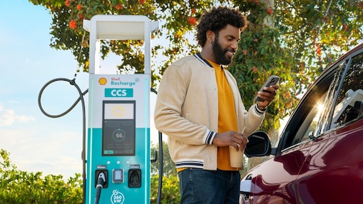 Man standing outside of his car looking at his phone while his car is charging.