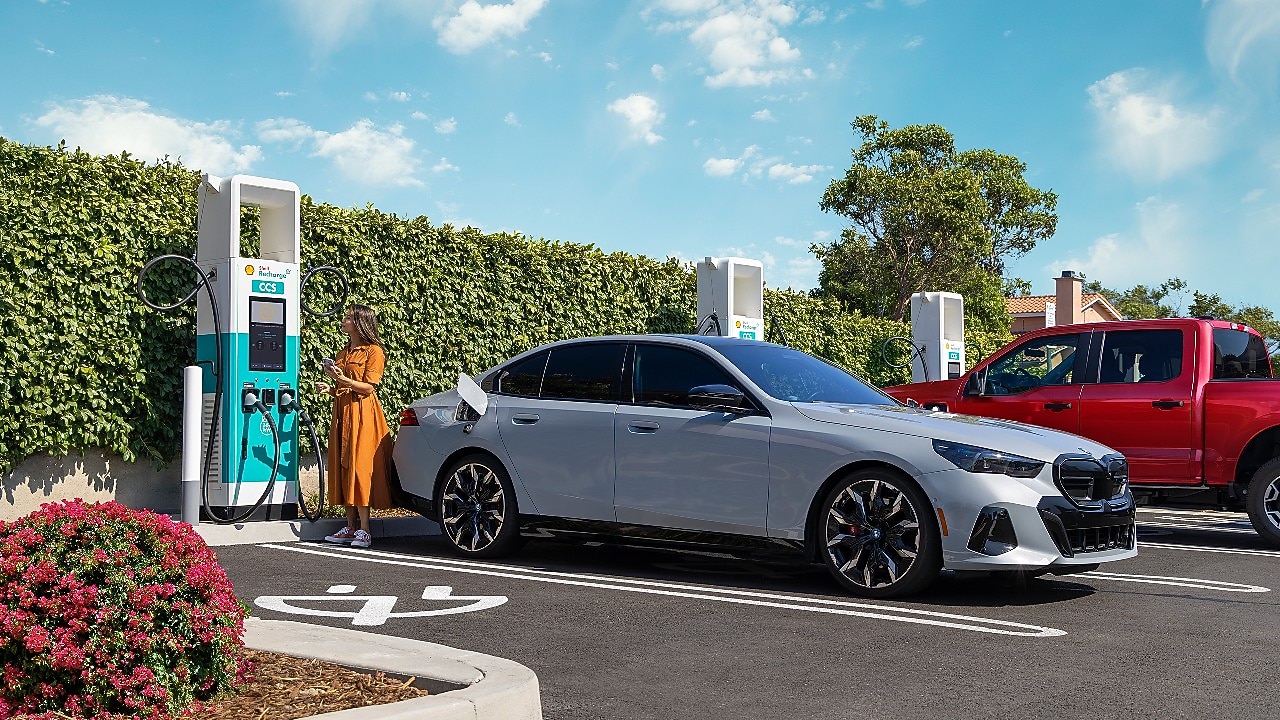 Woman standing outside her car with her phone in her hand and looking at the charging station screen.