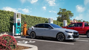 Woman standing outside her car with her phone in her hand and looking at the charging station screen.