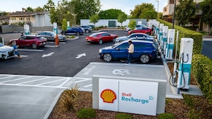 Elevated view of a Shell Recharge charging hub with multiple cars charging and drivers walking around the site.