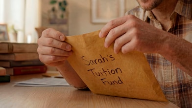 man holding orange envelope with sarah's tuition fund written on it
