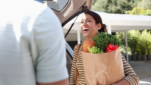 Woman seen talking to a companion, smiling and laughing whilst loading her shopping into her car